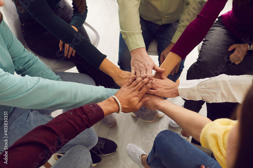Fototapeta Naklejka Na Ścianę i Meble -  Mixed race people sitting in circle and putting hands together in business team meeting or group therapy session. Community, trust, success, motivation, mutual responsibility, unity, support concepts