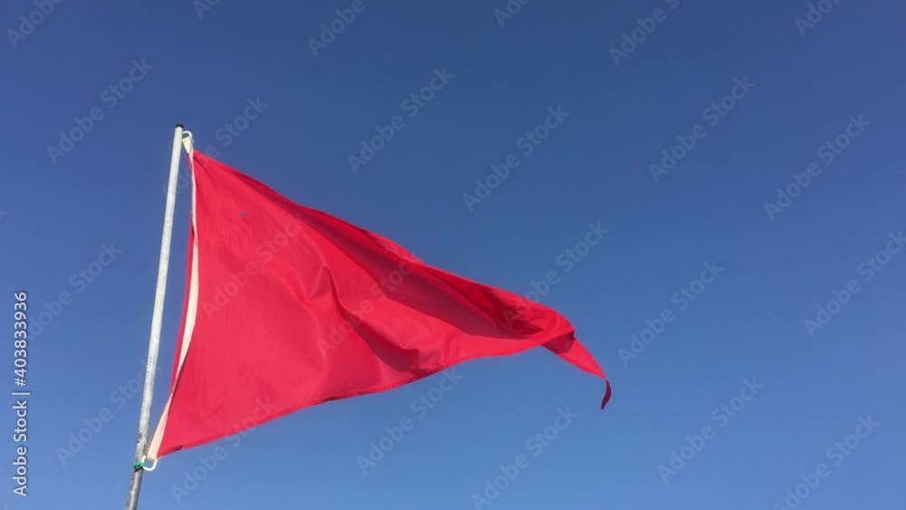 Un drapeau rouge flotte au vent au bord d’une plage pour indiquer que la mer est dangereuse et que la baignade est interdite.