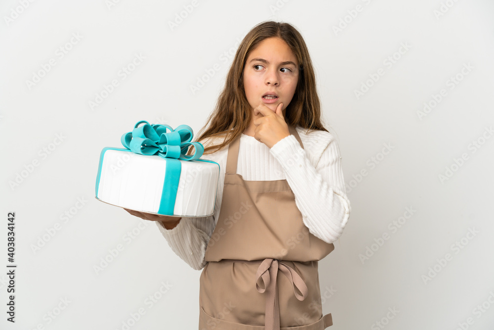 Little girl holding a big cake over isolated white background having doubts Little girl holding a big cake over isolated white background having doubts