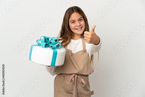 Little girl holding a big cake over isolated white background with thumbs up because something good has happened