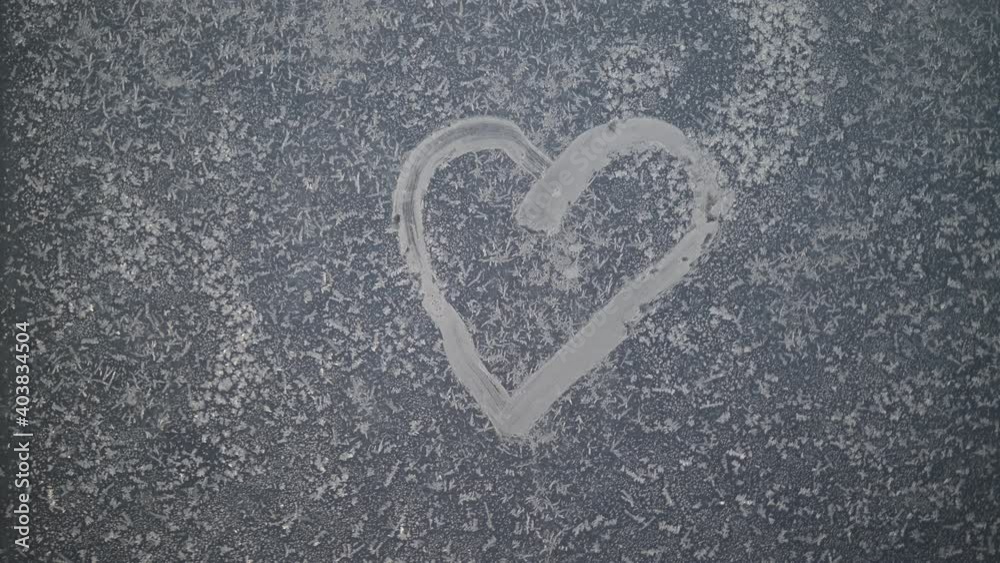 A heart drawn on a frozen winter window at sunset. A heart drawn on a frozen winter window at sunset.