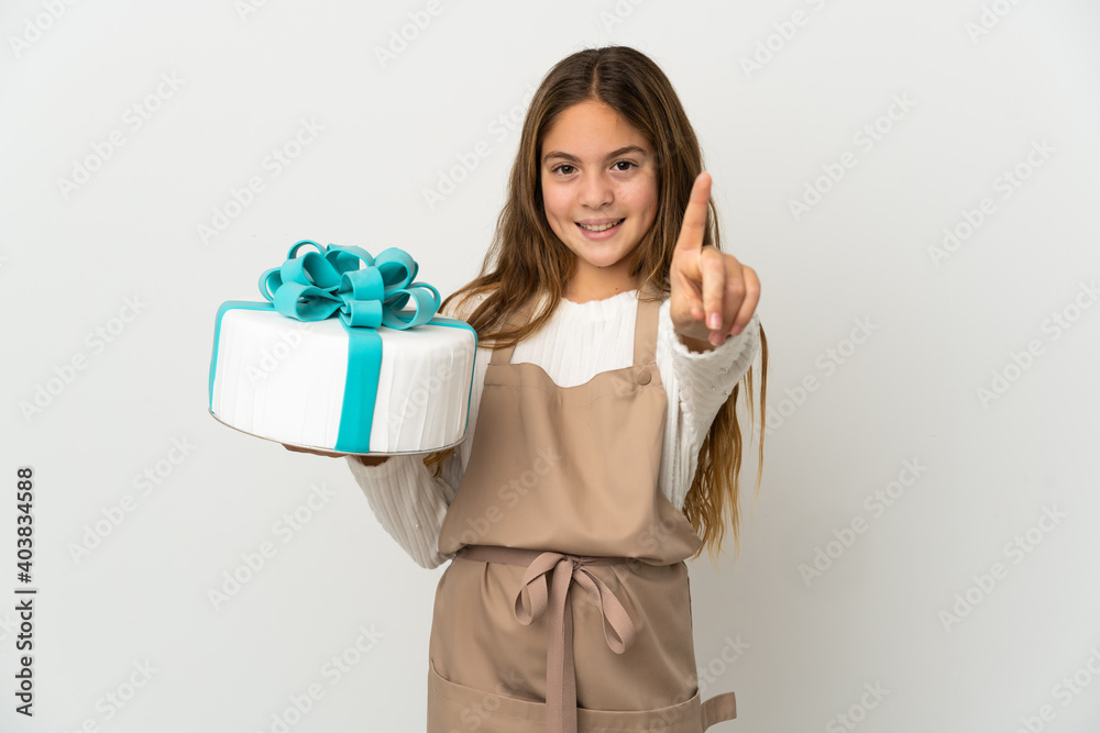 Little girl holding a big cake over isolated white background showing and lifting a finger