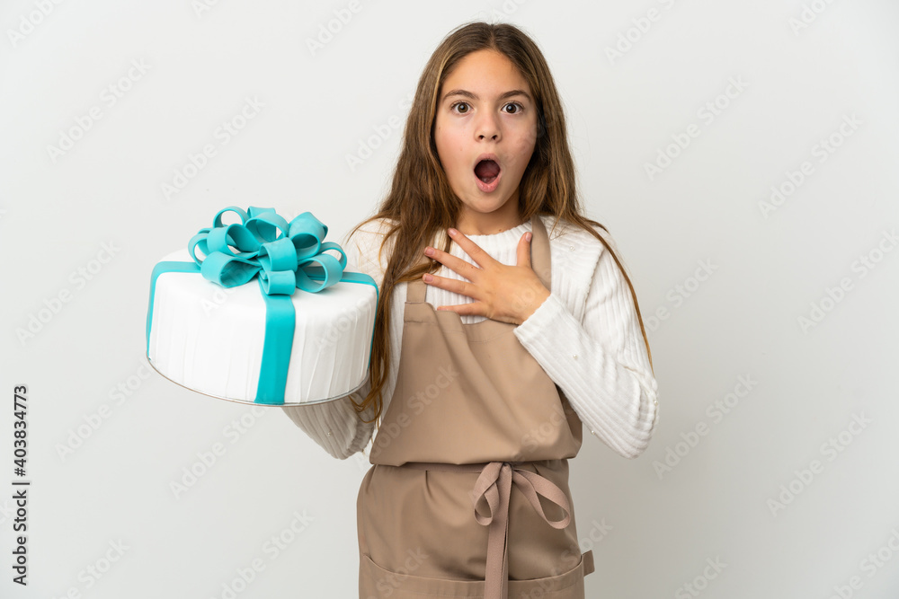 Little girl holding a big cake over isolated white background surprised and shocked while looking right Little girl holding a big cake over isolated white background surprised and shocked while looking right