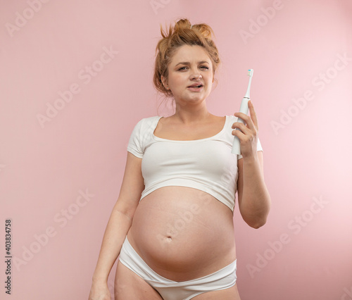 Young pregnant woman with a  toothbrush on a pink background. 
