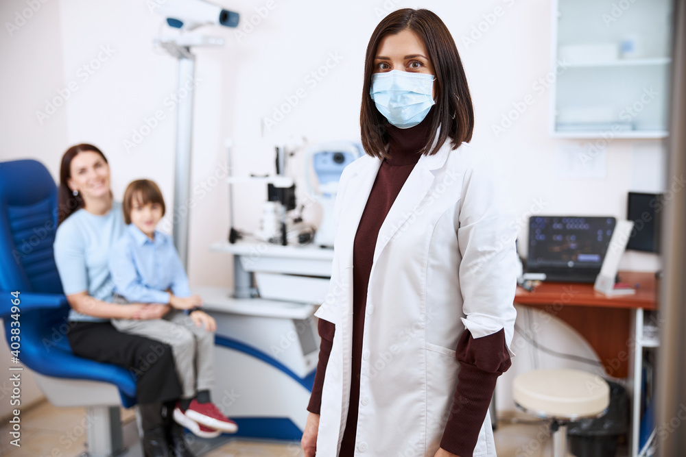 Optician wearing a medical mask and standing in her office Optician wearing a medical mask and standing in her office