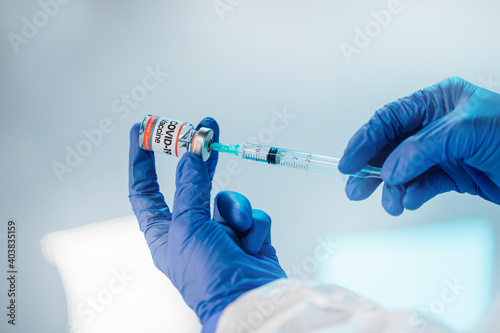 Doctor hands with rubber surgical gloves holding disposable plastic syringe while drawing the liquid from a Covid-19 vaccine vial bottle, at an Hospital or researcher lab.