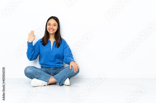 Young mixed race woman sitting on the floor isolated on white background saluting with hand with happy expression