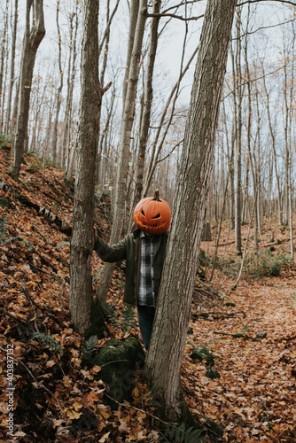 Man wearing scary carved pumpkin head in the woods for Halloween.