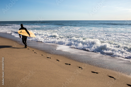 A surfer in wetsuit from behind carrying surfboard at Whitecrest Beach photo