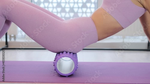 Sports woman in sportswear at home in the morning doing massage with a roller massager, stretching, kneading joints and spine    