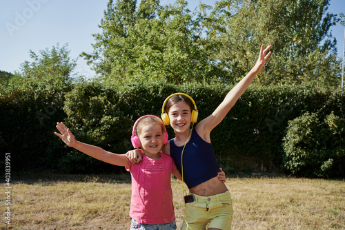 Little girls hugging and listening to music with yellow and pink headphones in the garden. Summer concept photo