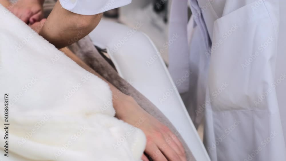 A young girl client with an alginate mask on her face lies on the cosmetology table, the beautician makes a manual hand massage A young girl client with an alginate mask on her face lies on the cosmetology table, the beautician makes a manual hand massage