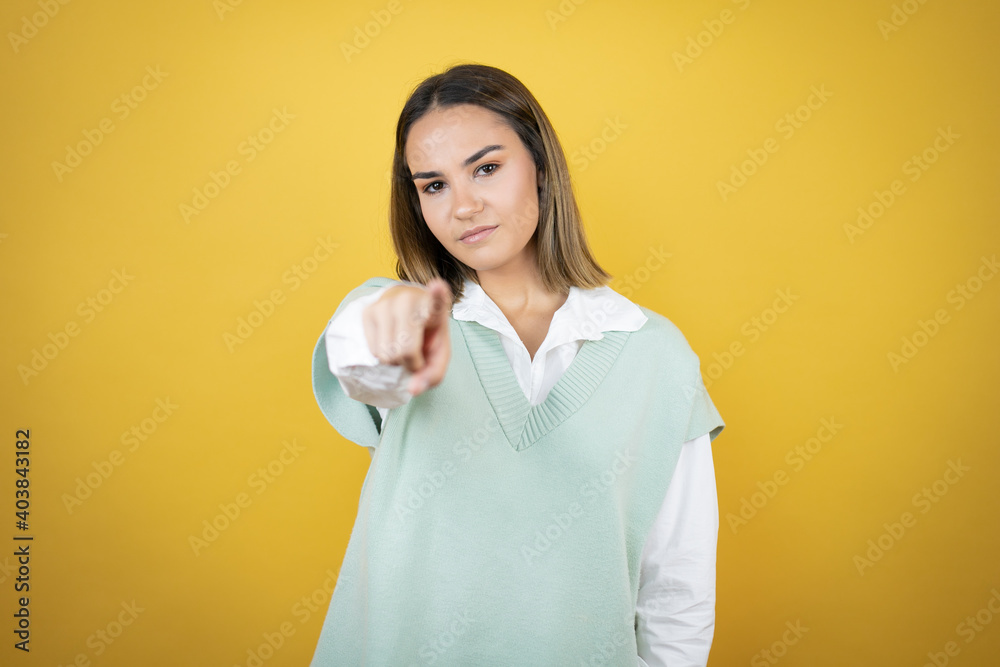 Pretty young woman standing over yellow background pointing to the front with finger Pretty young woman standing over yellow background pointing to the front with finger