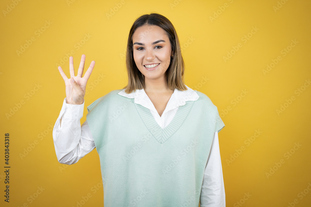 Pretty young woman standing over yellow background showing and pointing up with fingers number four while smiling confident and happy Pretty young woman standing over yellow background showing and pointing up with fingers number four while smiling confident and happy