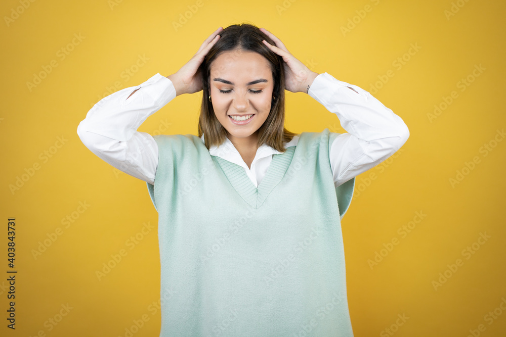 Pretty young woman standing over yellow background suffering from headache desperate and stressed because pain and migraine with her hands on head Pretty young woman standing over yellow background suffering from headache desperate and stressed because pain and migraine with her hands on head