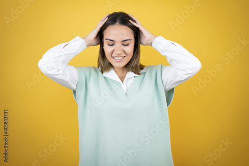 Pretty young woman standing over yellow background suffering from headache desperate and stressed because pain and migraine with her hands on head © Irene