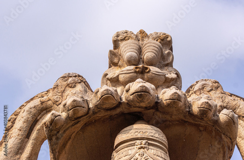 Hampi, Karnataka, India - November 5, 2013: Lakshmi Narasimha Temple. Closeup of brown stone hood on head of the god presenting the 7 snakes under blue sky.