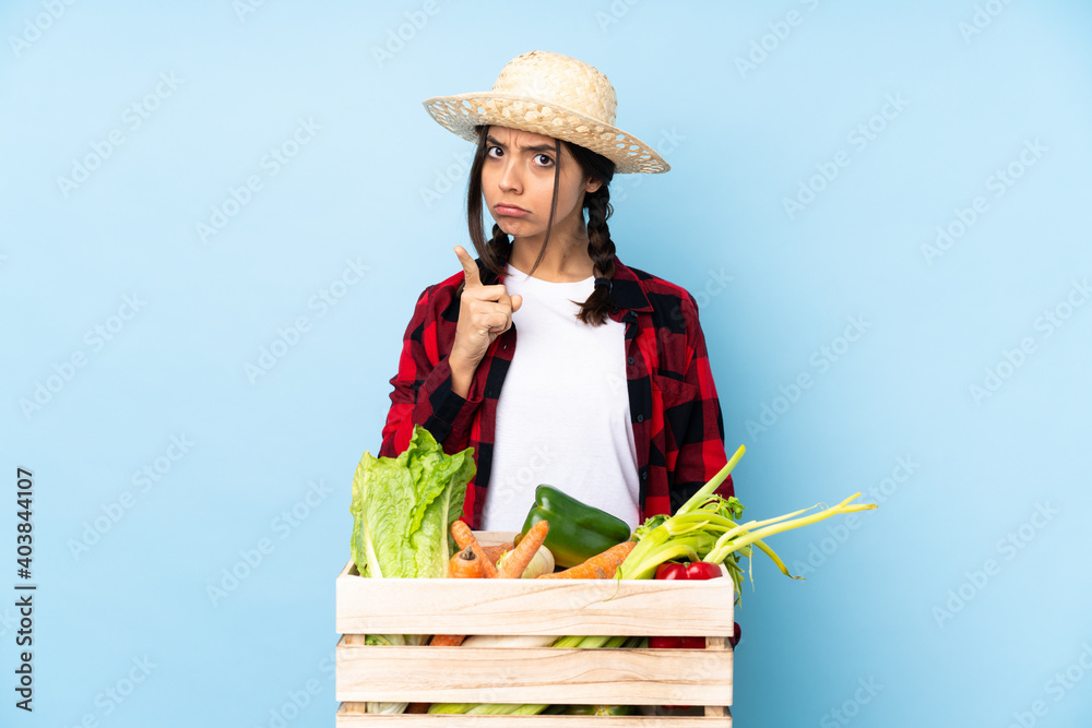 Young farmer Woman holding fresh vegetables in a wooden basket frustrated and pointing to the front