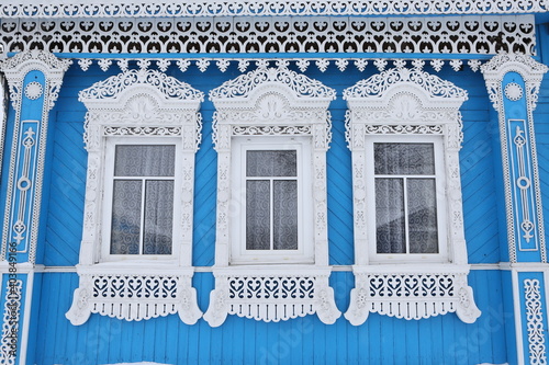 Ornamental windows with carved frames on vintage blue wooden rural house in Dunilovo village, Ivanovo region, Russia. Building facade. Russian traditional national folk style in wooden architecture photo