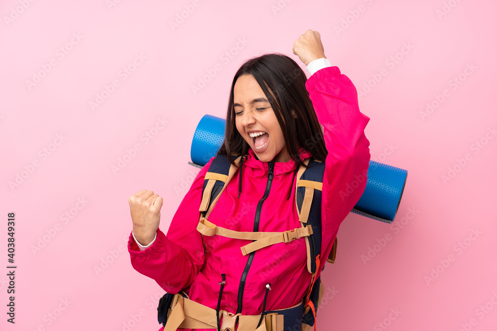 Young mountaineer girl with a big backpack over isolated pink background celebrating a victory Young mountaineer girl with a big backpack over isolated pink background celebrating a victory