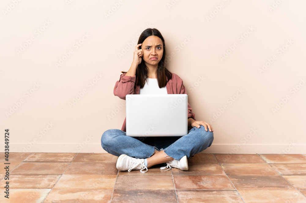 Young mixed race woman with a laptop sitting on the floor thinking an idea Young mixed race woman with a laptop sitting on the floor thinking an idea