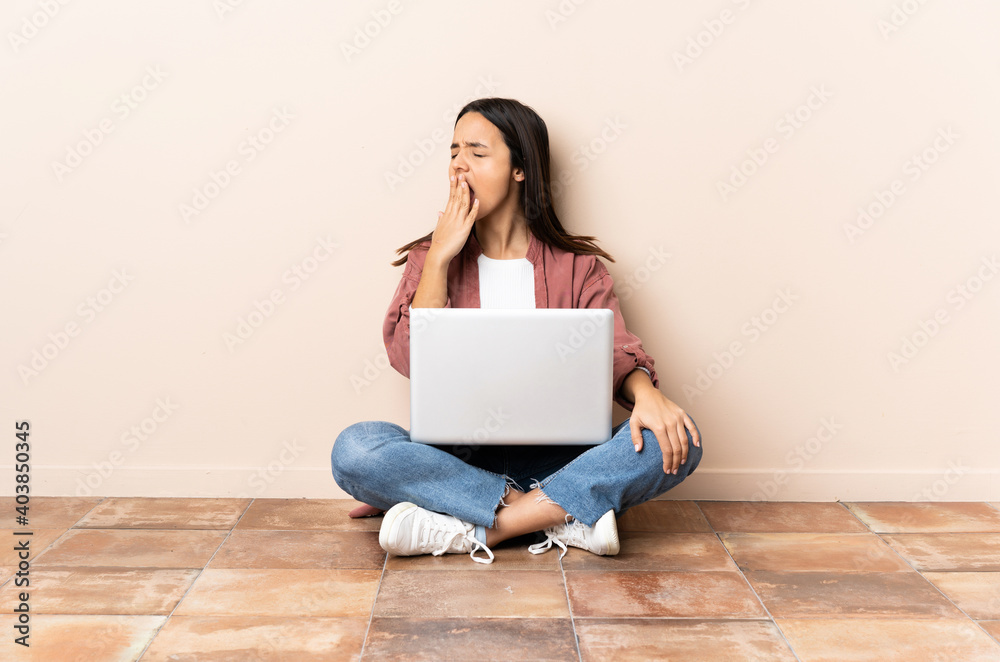 Young mixed race woman with a laptop sitting on the floor yawning and covering wide open mouth with hand Young mixed race woman with a laptop sitting on the floor yawning and covering wide open mouth with hand