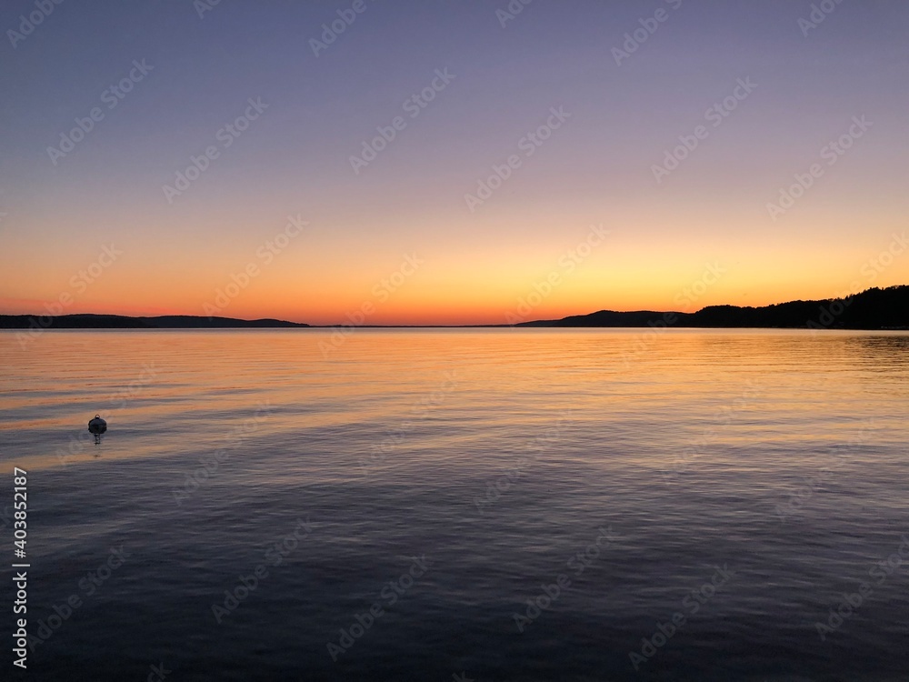 Purple and orange calm sunset above water with hills