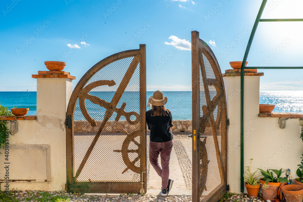 woman with straw hat looking at the sea leaning on a wooden door