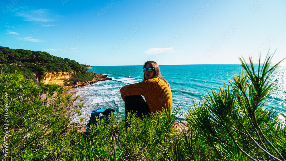 Fototapeta premium Freedom Young Girl Sitting on the Edge of Cliff hearing Wind near Blue Sea Alone. Love and Success Concept