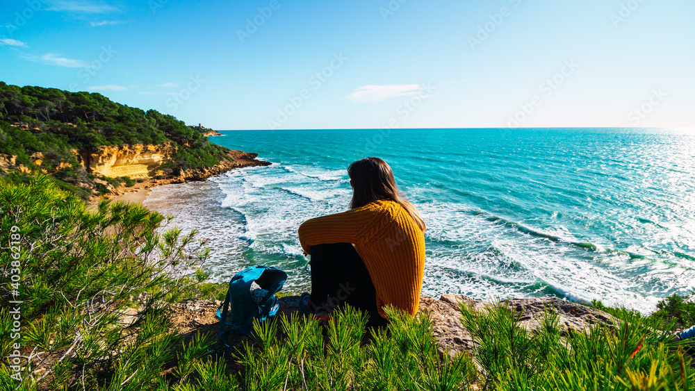 Freedom Young Girl Sitting on the Edge of Cliff hearing Wind near Blue Sea Alone. Love and Success Concept