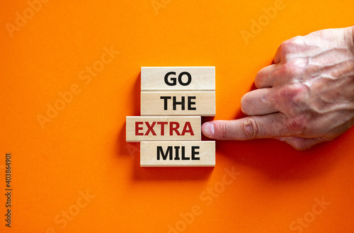 Go the extra mile symbol. Wooden blocks with words 'Go the extra mile'. Male hand. Beautiful orange background. Business and go the extra mile concept. Copy space. photo