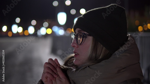 Russian girl freezes in the cold. A woman without gloves in winter rubs her palms and blows warm air out of her mouth to keep warm