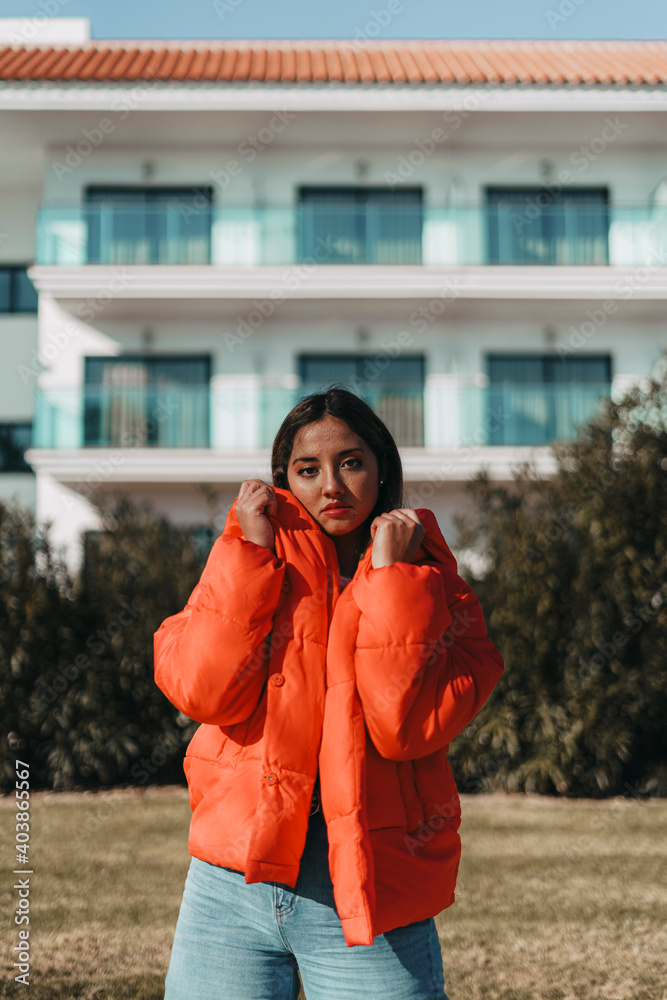 Fototapeta premium Chica joven adolescente mujer con abrigo naranja invierno con la playa de fondo y palmeras