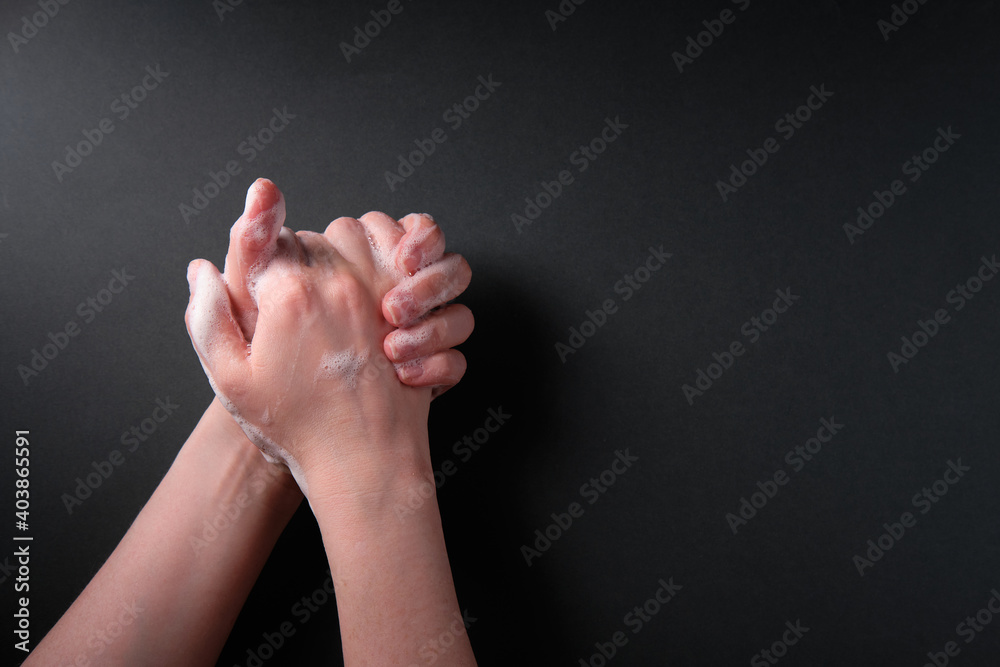 The girl washes her hands with soap, on a dark background, place for an inscription The girl washes her hands with soap, on a dark background, place for an inscription
