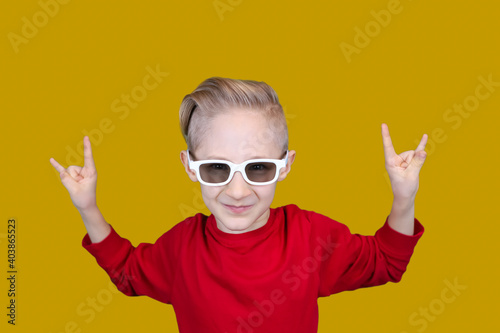 cool child in red clothes and glasses shows hand gestures on a yellow background