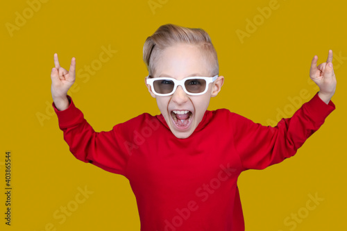 cool child in red clothes and glasses shows hand gestures on a yellow background © Roman