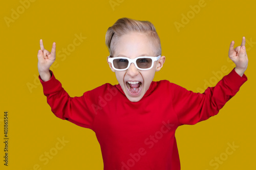 cool child in red clothes and glasses shows hand gestures on a yellow background