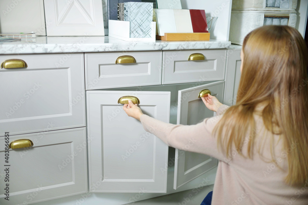 Home improvement concept. young girl designer opens a drawer of a kitchen cabinet in a shop salon. Home improvement concept. young girl designer opens a drawer of a kitchen cabinet in a shop salon.