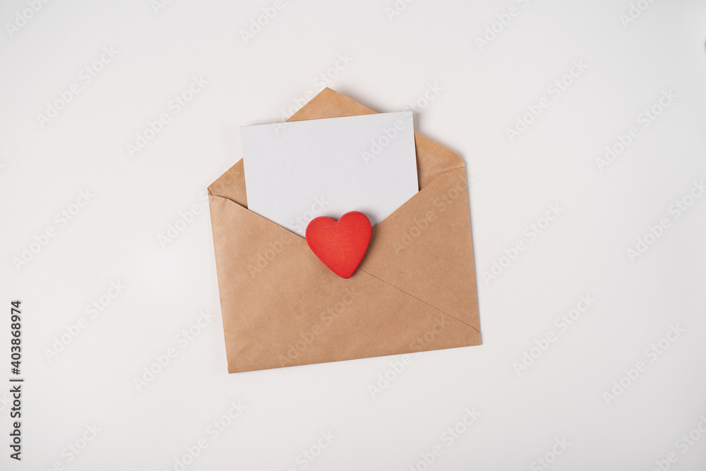 Craft envelope with a blank sheet inside and red wooden heart on the light (white) background. Flat lay, top view, space for text. Romantic love letter for Valentine's day concept. Craft envelope with a blank sheet inside and red wooden heart on the light (white) background. Flat lay, top view, space for text. Romantic love letter for Valentine's day concept.