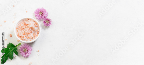 Long wide banner with fresh organic Himalaya salt in a bowl with aromatic purple flowers and green leaves on white marble background. Spa and wellness banner concept. 