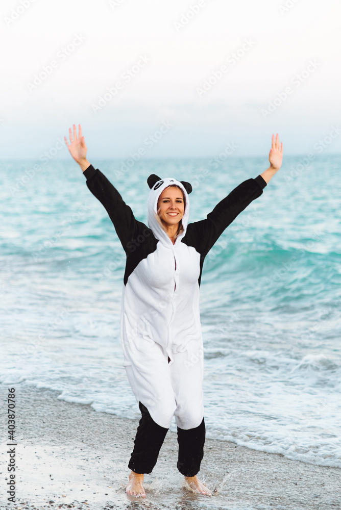 Emotional girl wears kigurumi laughing in front of the camera. Adorable young woman by the sea in panda pajamas dancing Emotional girl wears kigurumi laughing in front of the camera. Adorable young woman by the sea in panda pajamas dancing