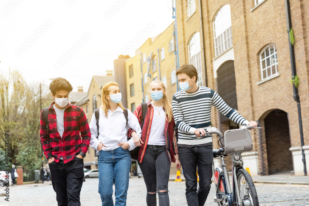 Obraz premium Teen group of friends wearing face masks and walking in the city - Multiracial group of teenagers best friends enjoying time together in London during coronavirus - Lifestyle and friendship in London