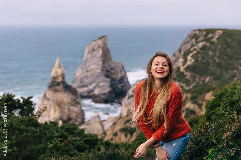 Naklejka premium Happy tourist girl standing on the edge of a cliff against the backdrop of a beautiful view of the sea and the beach.