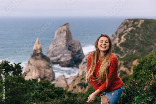 Happy tourist girl standing on the edge of a cliff against the backdrop of a beautiful view of the sea and the beach. © Ivan