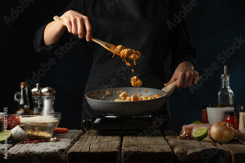 Photography Chef in black uniform stir frying chicken fillet in the pan