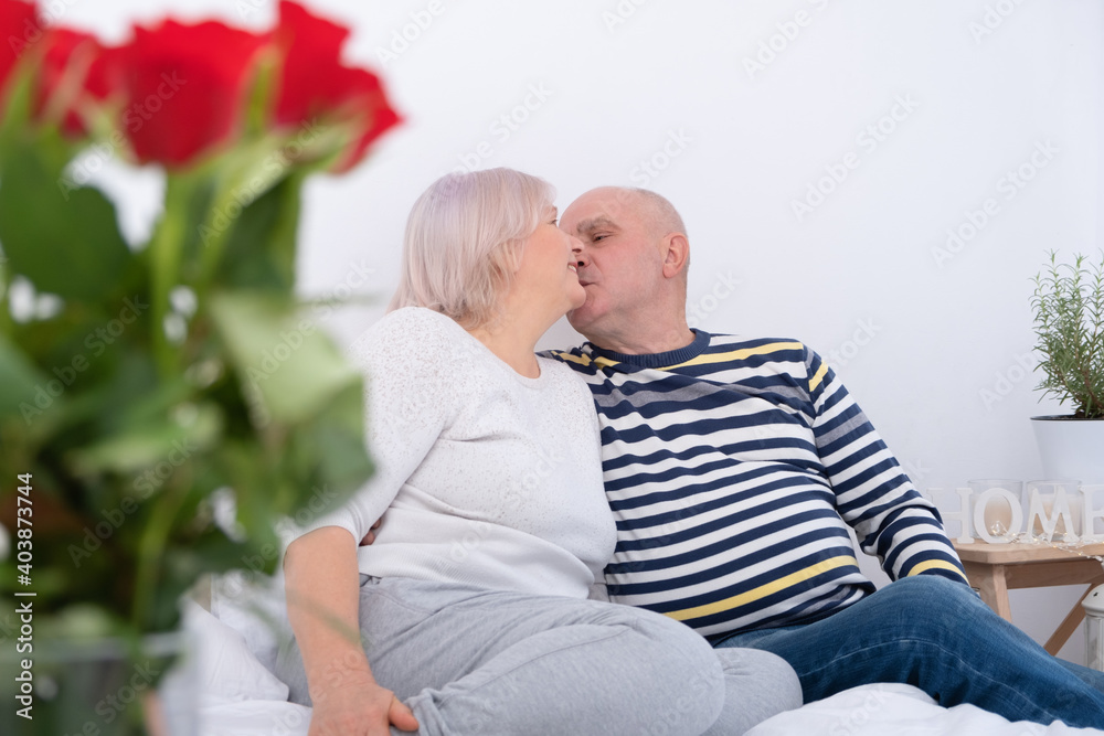romantic senior couple kissing on bed. bouquet of roses romantic senior couple kissing on bed. bouquet of roses