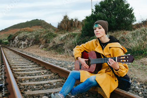 Young woman in yellow coat playing the guitar sitting on the train tracks. youth and music. way of living. wanderlust