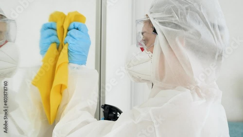 Bacteriologist or cleaning worker in bioazard protective suit washing house with chemical detergent and desinfecting furniture photo