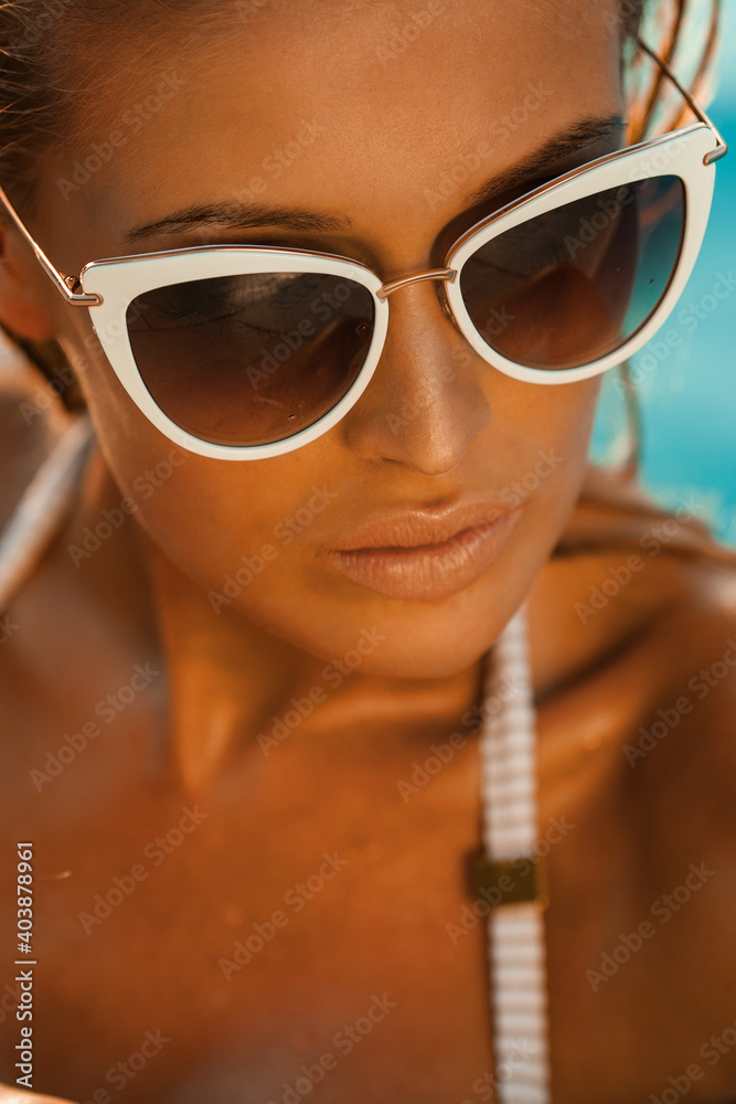 Beautiful sexy blonde woman with long hair and tanned body wearing swimsuit and sunglasses posing at the swimming pool.