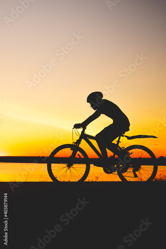 Unrecognizable silhouette man riding bicycle against sunset sky. Road biking cyclist workout, riding racing bicycle on open road. Workout for triathlon. Dramatic sunset background. Copy space
